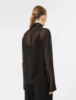 Back view of a woman wearing a sheer black blouse with a high neck and long sleeves, her hair in a low ponytail.