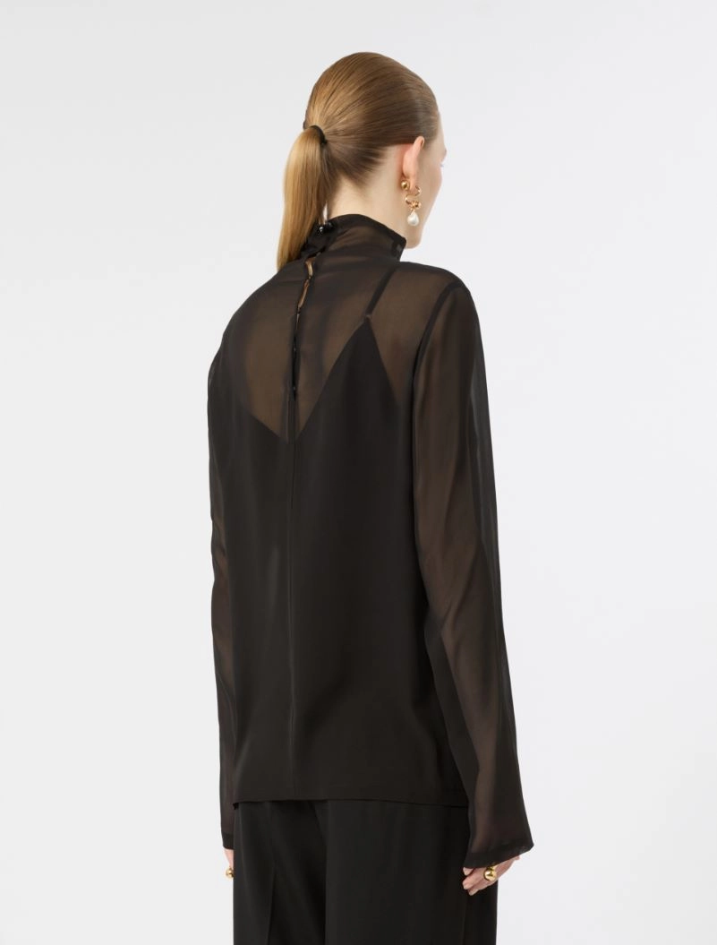 IMG_3775 - New Trend Back view of a woman wearing a sheer black blouse with a high neck and long sleeves, her hair in a low ponytail.