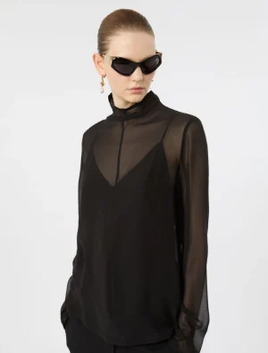 Model wearing a black sheer blouse with high neck and layered front, paired with oversized black sunglasses and gold earrings.