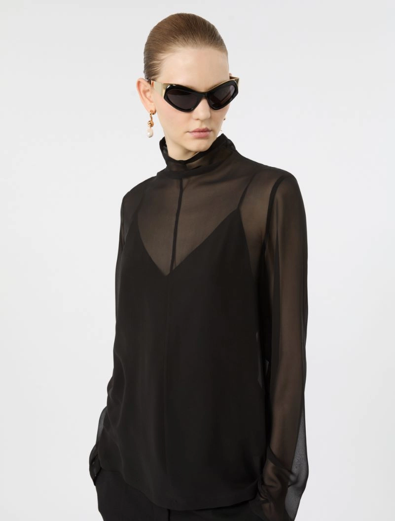 IMG_3776 - New Trend Model wearing a black sheer blouse with high neck and layered front, paired with oversized black sunglasses and gold earrings.