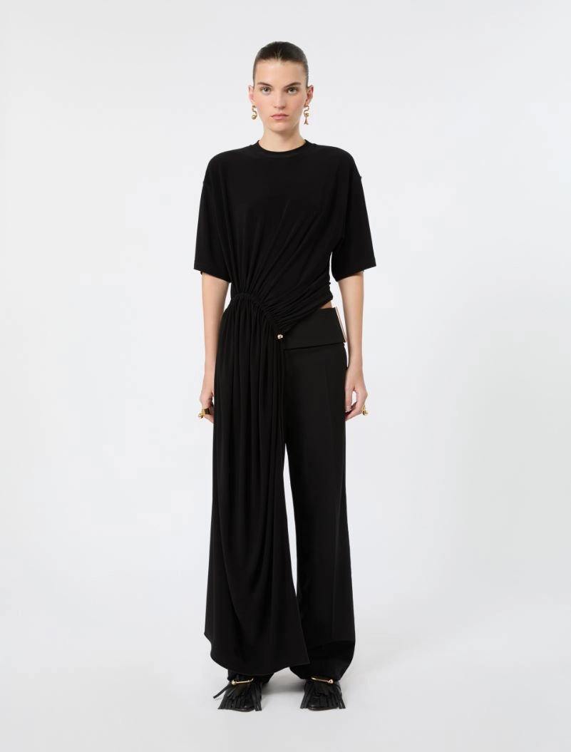 IMG_3780 - New Trend Model wearing a black draped jumpsuit with a knot at the waist and wide legs, standing against a white background.