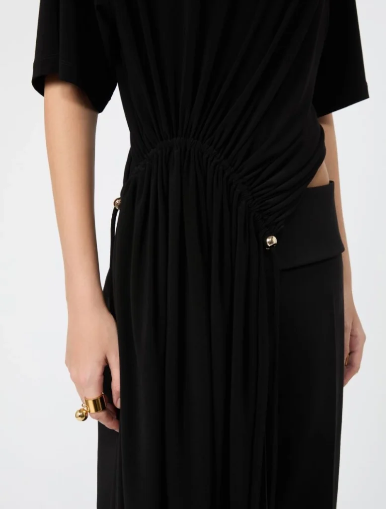 Close-up of a black dress showing a gathered ruched waist with a side pocket and subtle gold hardware.