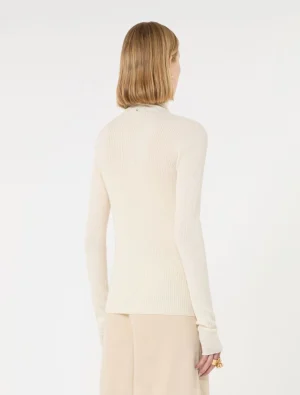Back view of a woman wearing a cream ribbed turtleneck sweater and a beige skirt; shoulder-length blonde hair visible from behind.