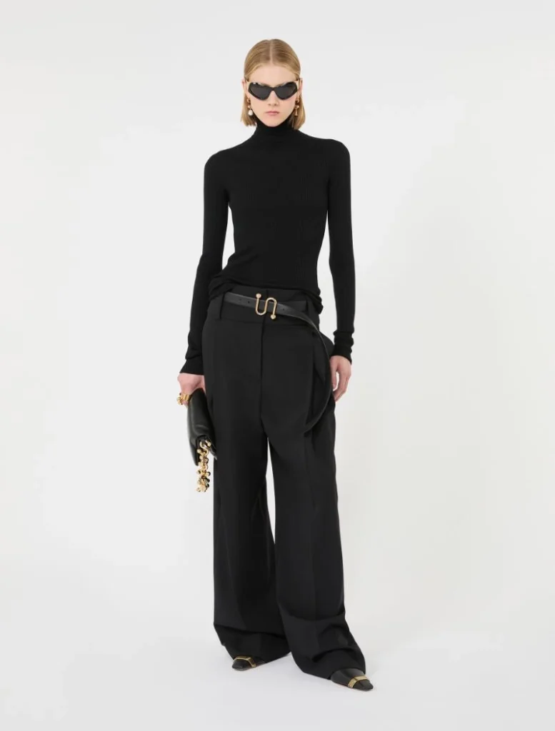 Model in an all-black outfit: black turtleneck, wide-leg trousers, gold belt, black clutch, sunglasses.