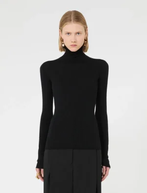 Front view of a model wearing a black ribbed turtleneck sweater and black trousers against a light background.
