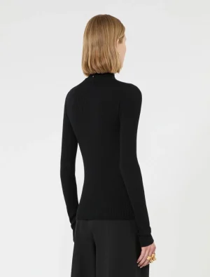 Back view of a person wearing a black ribbed turtleneck sweater and black wide-leg pants, blonde hair cut to the shoulders.