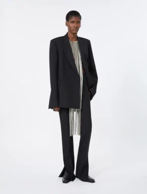 Model wearing an oversized black blazer over a silver-striped top with matching wide-leg pants, standing in a studio.