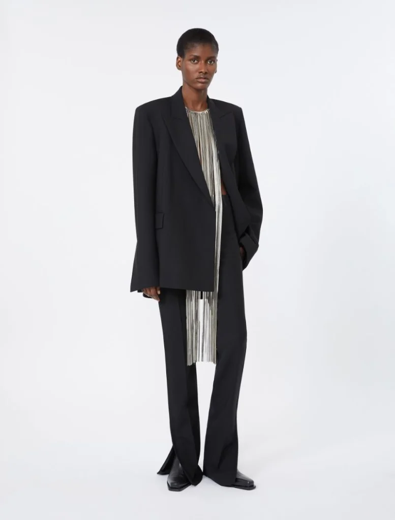 Model wearing an oversized black blazer over a silver-striped top with matching wide-leg pants, standing in a studio.