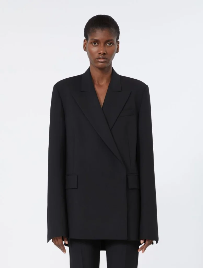 Model wearing an oversized black blazer with wide lapels and flap pockets, paired with matching black trousers against a white background.