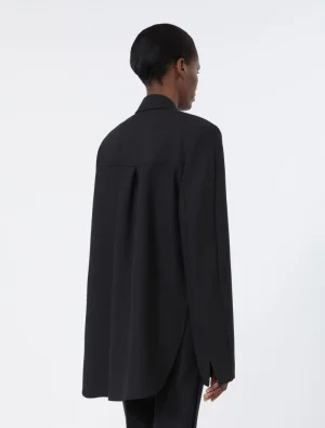 Back view of a person wearing a loose black blazer with a long curved hem and center back vent, standing against a light background