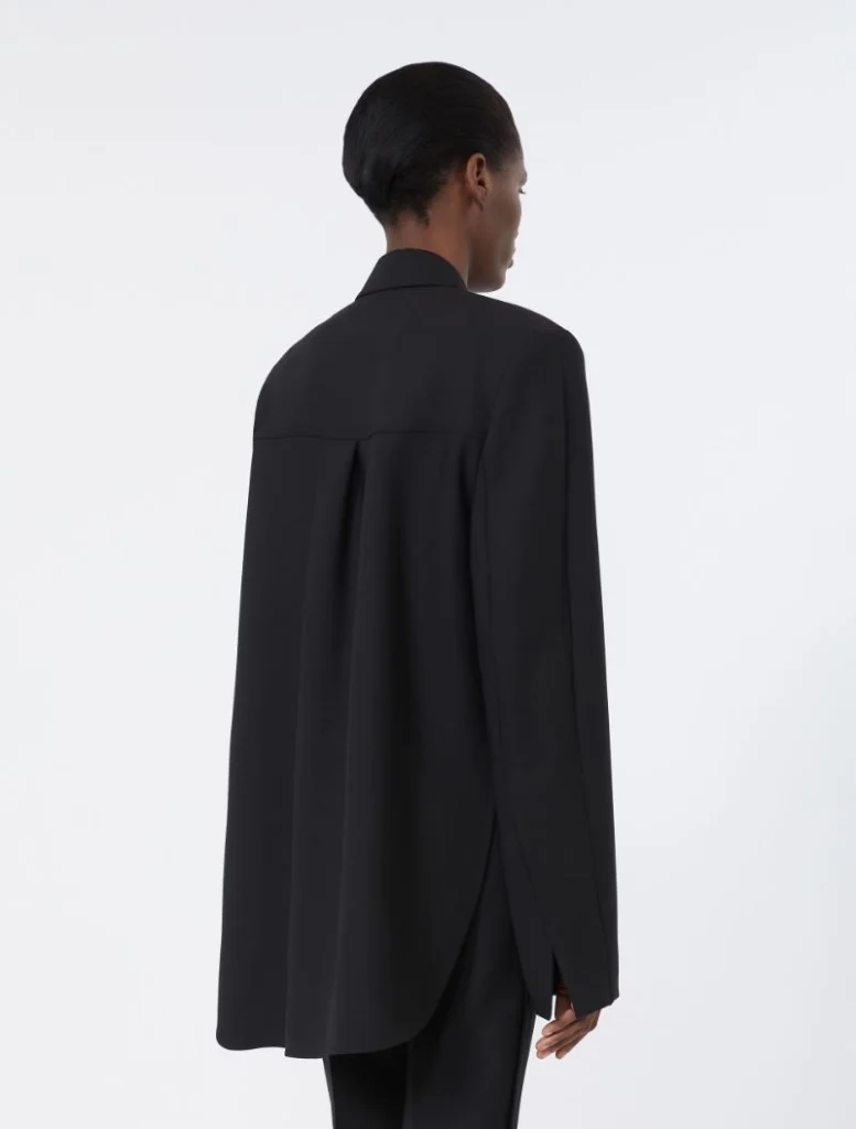 Back view of a person wearing a loose black blazer with a long curved hem and center back vent, standing against a light background