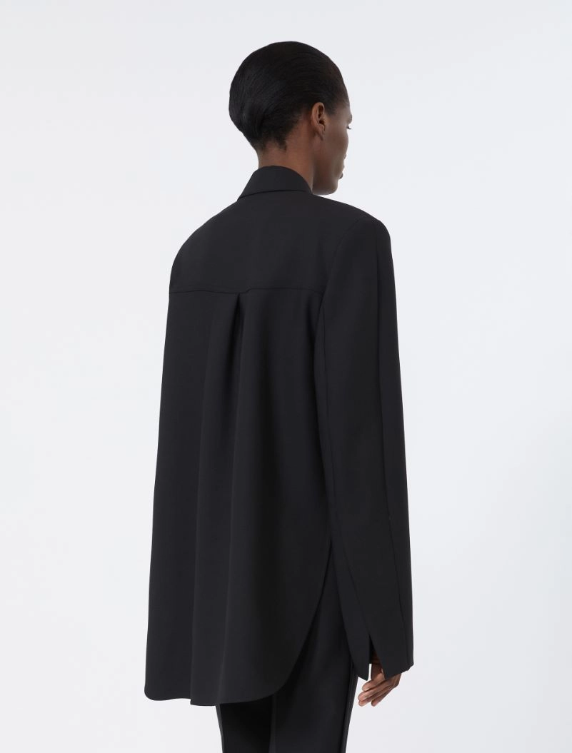 IMG_3798 - New Trend Back view of a person wearing a loose black blazer with a long curved hem and center back vent, standing against a light background