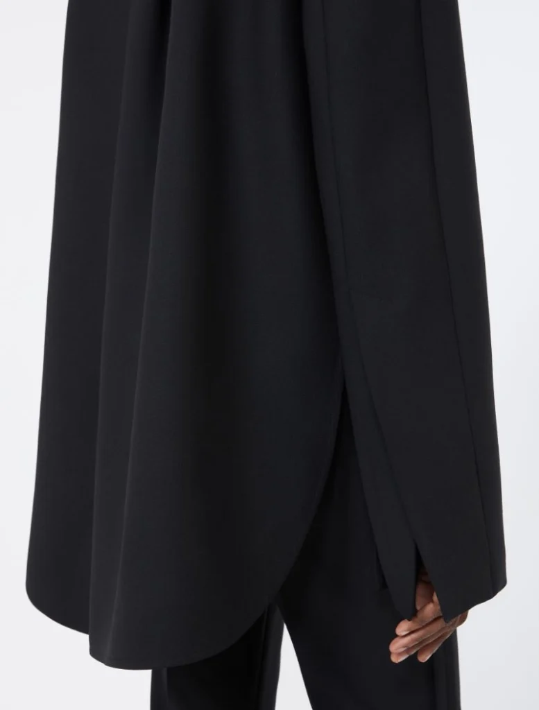 Close-up of a black draped coat or cape with a curved hem and side vent over black pants.