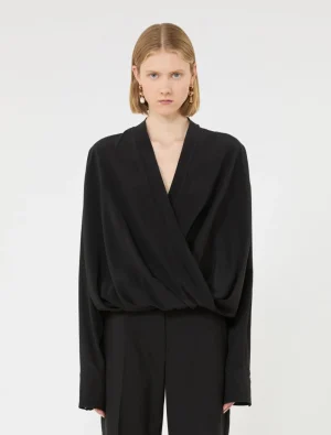 Young woman wearing a black draped wrap blouse with wide sleeves and matching black pants, neutral studio backdrop
