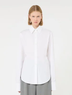 Model wearing a white button-down shirt with long sleeves and a curved hem, paired with gray trousers, facing the camera.