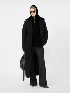 Model in an all-black, oversized coat with hood, sunglasses, and a black handbag for a high-fashion look.