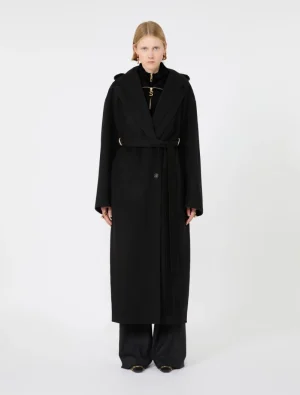 Female model wearing a long black belted wrap coat with oversized sleeves, paired with wide-leg black trousers.