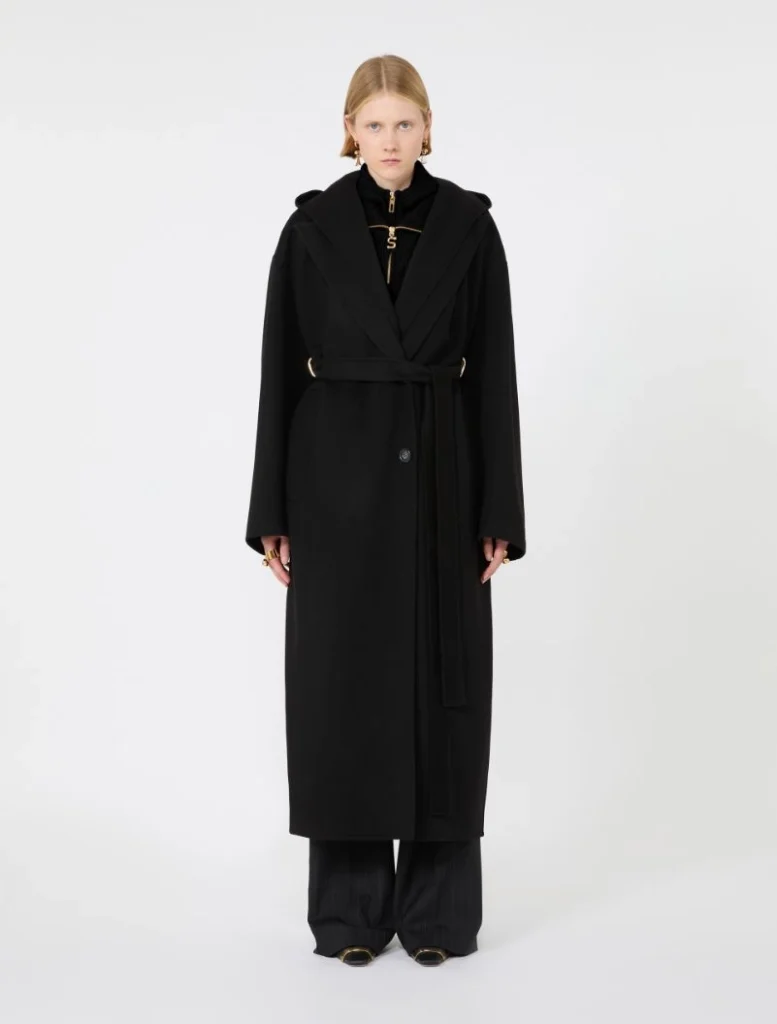 Female model wearing a long black belted wrap coat with oversized sleeves, paired with wide-leg black trousers.
