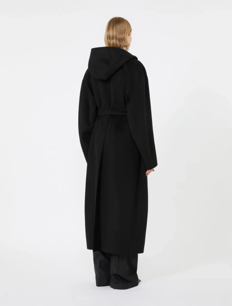 Back view of a person wearing a long black hooded coat with a belt, against a white background.