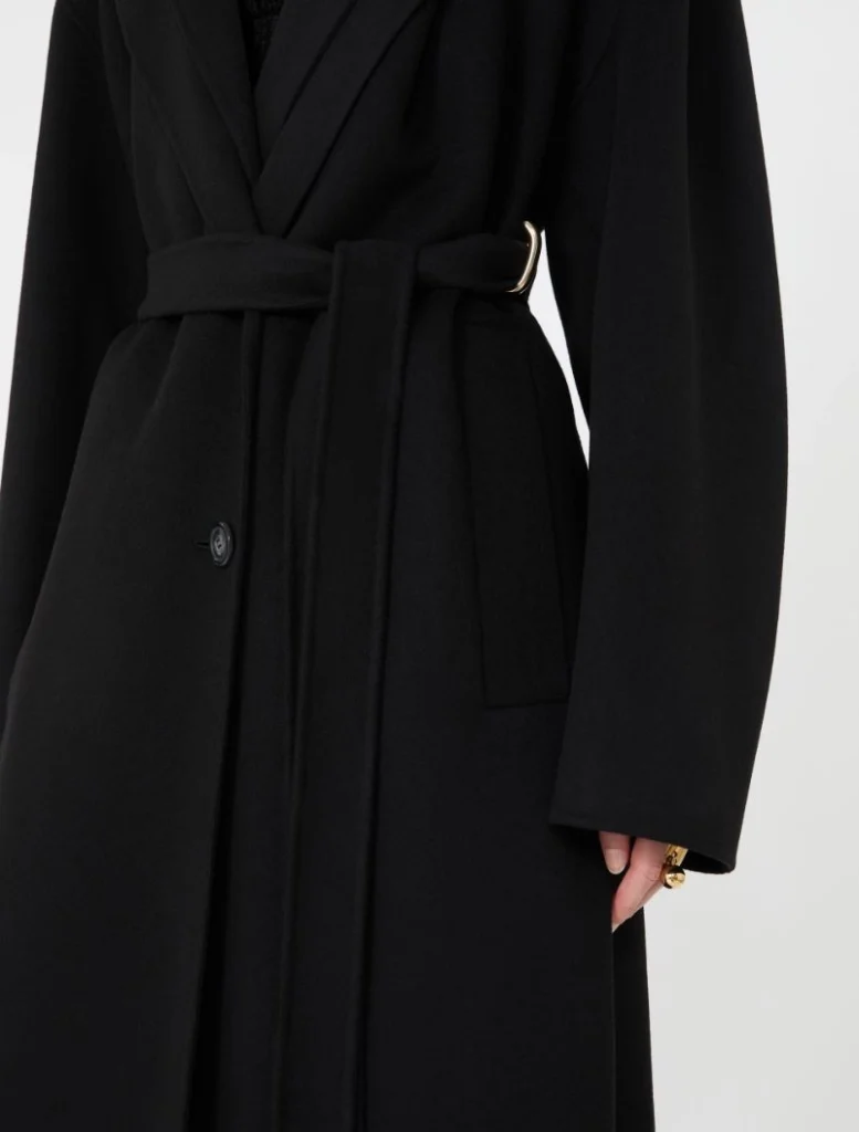 Close-up of a black belted coat tied at the waist with a gold-buckle belt looped over the front edge.