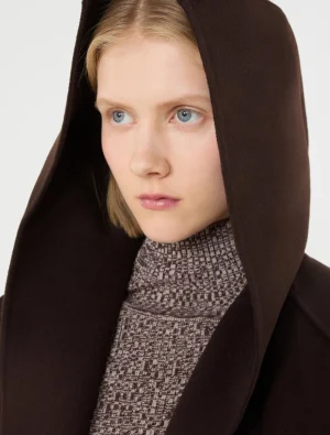 Young woman with blue eyes wearing a dark brown hooded coat and a patterned turtleneck, looking to the side.