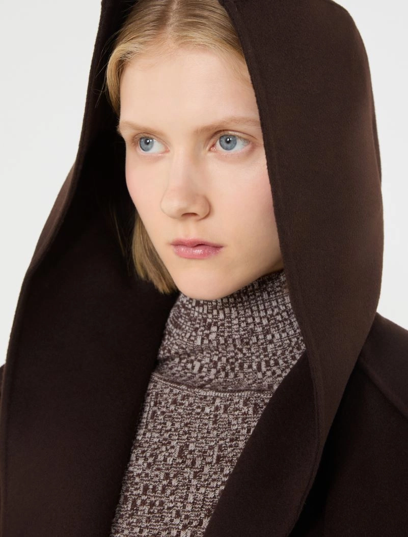 IMG_3822 - New Trend Young woman with blue eyes wearing a dark brown hooded coat and a patterned turtleneck, looking to the side.