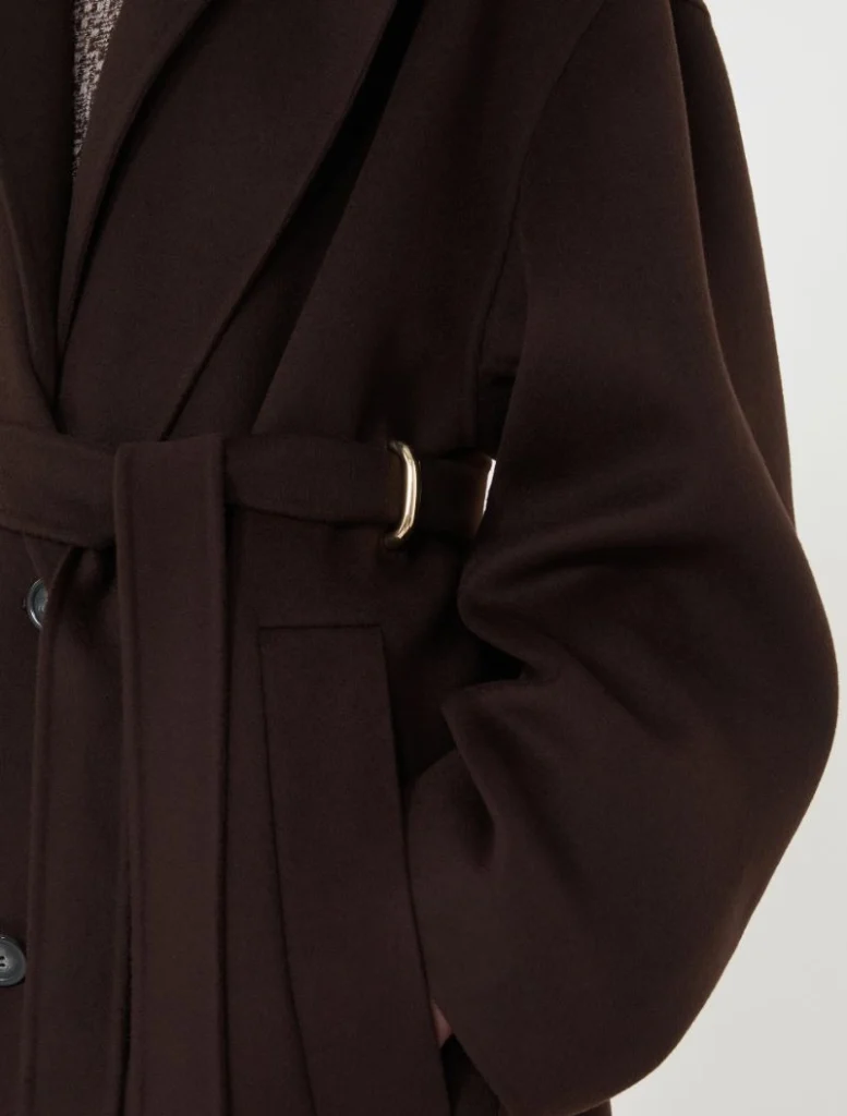 Close-up of a dark brown belted coat with a gold buckle and side pocket detail.