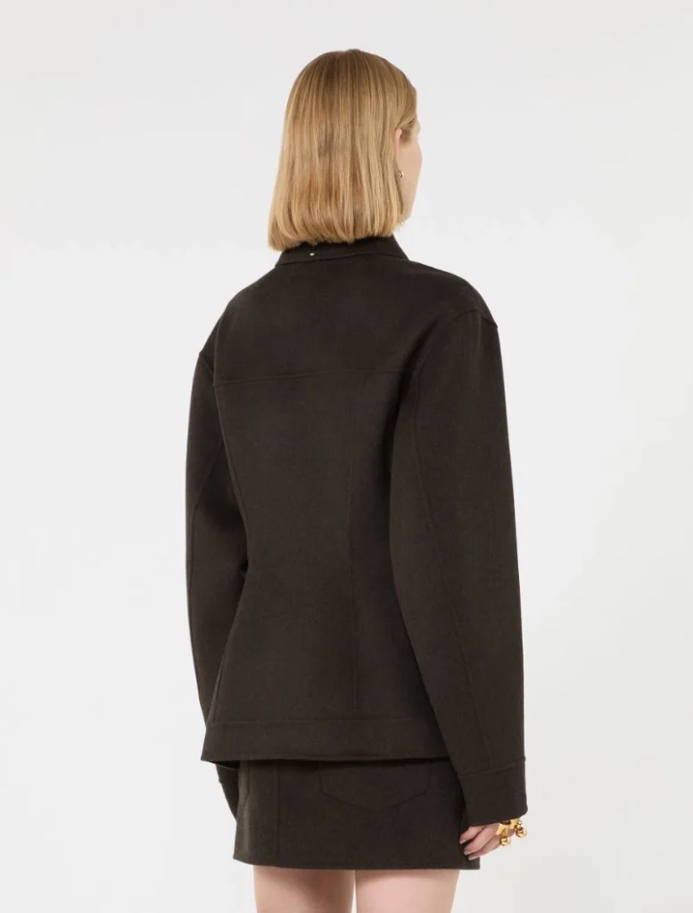 Back view of a person wearing a dark oversized jacket with a matching short skirt, blonde bob hairstyle visible from behind.