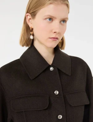 Woman wearing a dark wool coat with a large collar and silver buttons, accessorized with gold hoop earrings and a pearl drop.