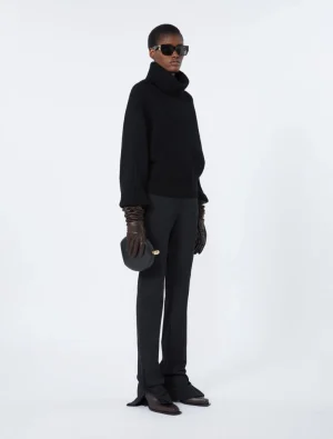 Model in an all-black ensemble: oversized turtleneck, wide-leg pants, brown gloves, sunglasses, and a small black handbag used as a fashion look.