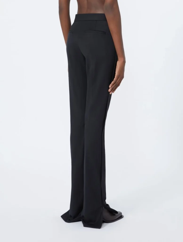 Back view of a person wearing black tailored wide-leg trousers with floor-length hem and back welt pockets