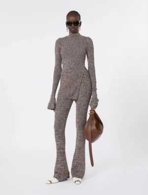 Model wearing a matching knit turtleneck and flared pants in taupe, accessorized with sunglasses and a brown handbag.