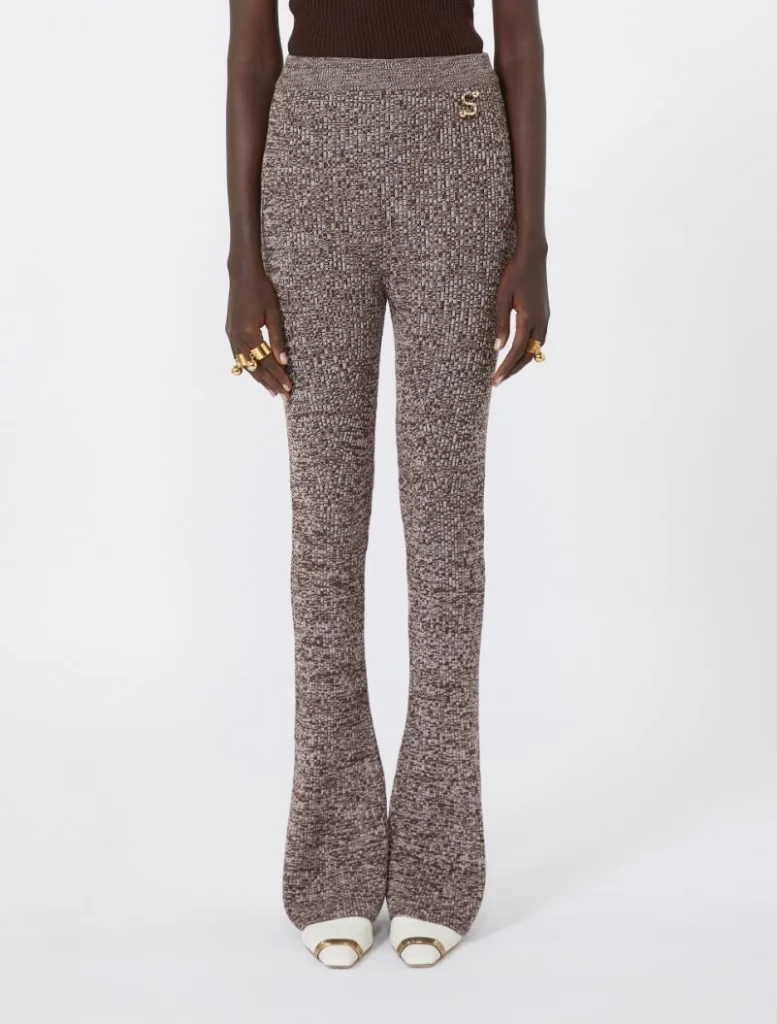 Full-length view of a person wearing brown speckled high-waisted flared pants and white shoes with gold hardware.