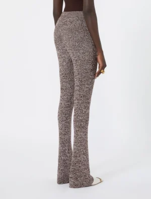 Back view of a person wearing textured brown speckled high-waisted knit flared pants, with a dark top and gold ring on the hand visible.