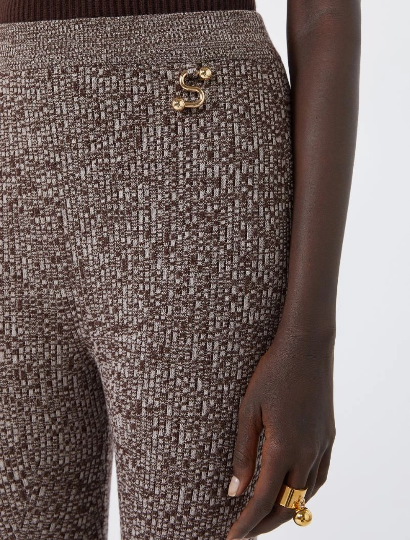 IMG_3844 - New Trend Close-up of brown tweed trousers with a gold S-shaped pin at the hip and a chunky gold ring on the wearer's finger.