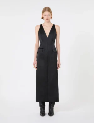 Model wearing a sleeveless black jumpsuit with a deep V-neck and front flap pockets, paired with black boots.