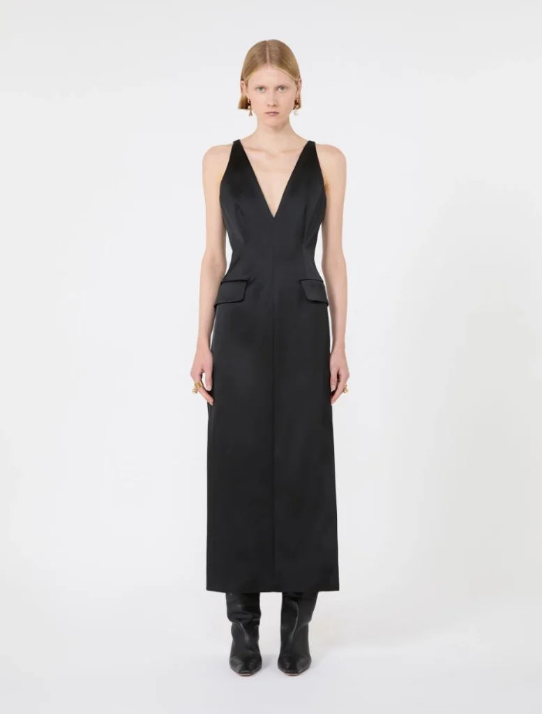 Model wearing a sleeveless black jumpsuit with a deep V-neck and front flap pockets, paired with black boots.