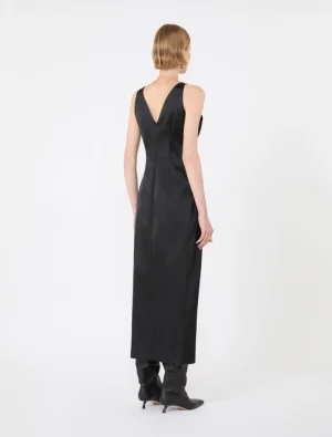 Back view of a model wearing a black sleeveless midi dress with a V-shaped back, paired with black heeled boots.