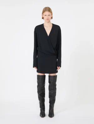 Front view of a model in a black V-neck wrap blouse, matching mini skirt, and tall black leather boots.