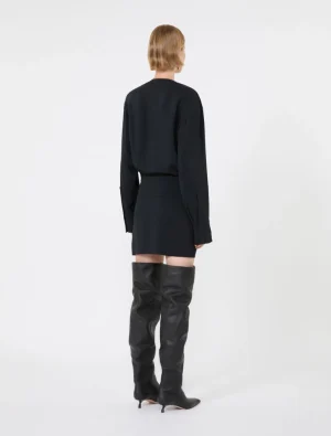 Back view of a person wearing a black long-sleeve blouse tucked into a black mini skirt, paired with over-the-knee black leather boots.