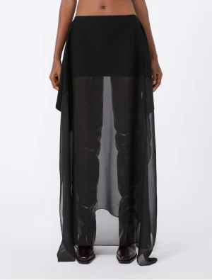 Black high-waisted skirt with a sheer, floor-length overlay over opaque pants, shown with dark boots.