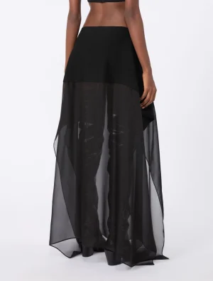 Back view of a model wearing a black two-tone maxi skirt: an opaque short underlayer and a sheer, floor-length overlay.