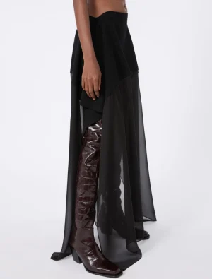 Outfit featuring a black layered sheer overskirt over a long black skirt paired with burgundy crocodile-embossed knee-high boots.