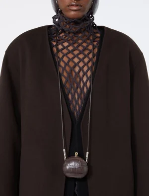 Model wearing a black mesh neckpiece over a black outfit, with a small round brown handbag hung at the chest.