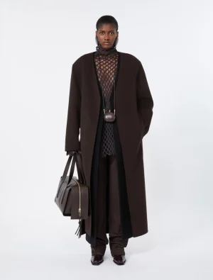 Model wearing a long dark brown coat over a black lattice top, carrying a brown structured handbag and wearing dark boots.