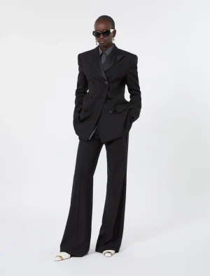 Person in an oversized black double-breasted suit with wide-leg trousers, striped shirt, sunglasses, and white sandals.