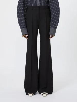 Full-length black wide-leg trousers with a pinstripe shirt, accessorized with gold rings and metallic-toe shoes.