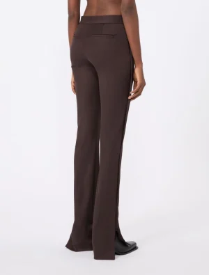 Back view of chocolate brown wide-leg trousers on a model, with a flat waistband and rear welt pocket, flaring slightly at the bottom with small side slits.