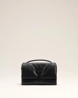Black leather handbag with a heart-shaped clasp displayed on a pale studio background.