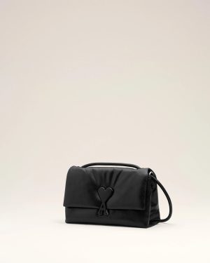 Black leather handbag with a heart-shaped clasp on a pale beige background.